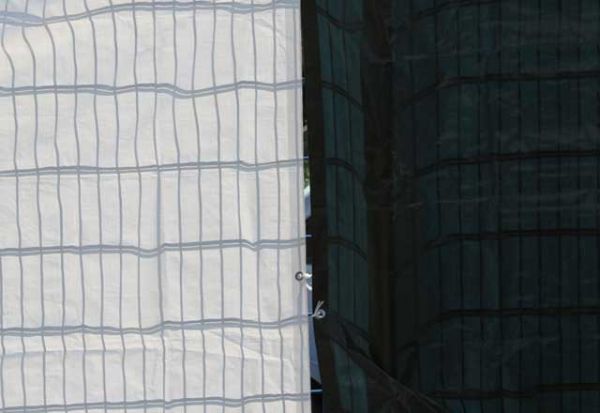 Lichtdurchlässigkeit Abdeckplane weiß und grün/blau aufgehängt am Zaun